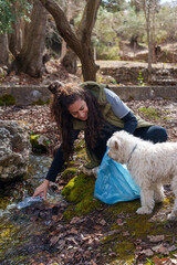 Volunteer cleaning plastic bottles from a forest stream while her dog joyfully assists in the...