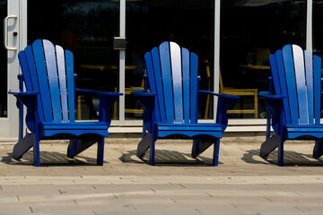 Three blue wooden outdoor chairs on the front porch of a business store