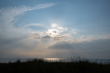 Dune grass by the sea with sun behind the clouds