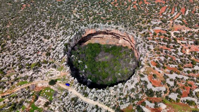 Lush greenery covering deep limestone sinkholes cennet and cehennem, revealing dramatic karst topography in mediterranean taurus mountain region near silifke, mersin