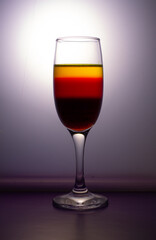 A glass of champagne with colorful liquid on grey background