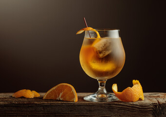 Old Fashioned cocktail with a ice, garnished with an orange peel on a old wooden board.