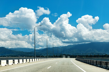 A highway stretches beneath a bridge, framed by majestic mountains in the background, showcasing a...
