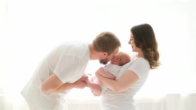 A happy young family mom dad and a small child smiling and kissing on a white isolated window background, a loving family threesome at home