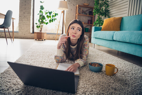 Young woman indoors studying and relaxing at home with laptop, sitting comfortably in modern living room