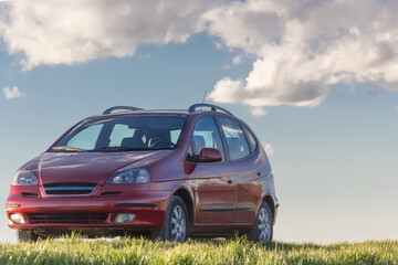 Red Monovolumen Car Parked on Grass Under a Bright Blue Sky