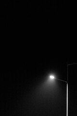 A solitary street lamp emits a bright white light, cutting through the darkness of the night.