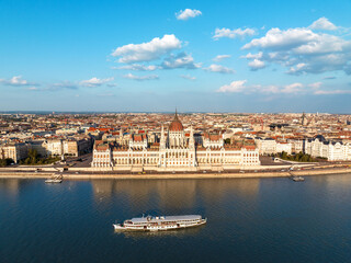 Fototapeta premium Residence of Hungarian Parliament, Budapest backdrop of sunset sunny day in summer. National symbol aerial view other bank of Danube River. Floating river pleasure passenger vessels. Travel concept