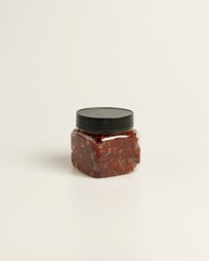 Glass jar with black lid containing spicy red chili paste on white background
