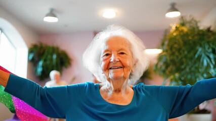 Happy elderly woman sitting, performing arm exercises with colorful ribbons, smiling and looking at camera, promoting active aging and rehabilitation in a bright retirement home or nursing facility