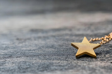 Gold star pendant on dark grey textured surface;  holiday, festive, celebration concept;  background bokeh effect; ideal for greeting cards or jewelry websites