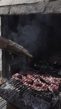 hand with gloved hand turning the meat wrapped in silver foil and the meat on a barbecue grill.