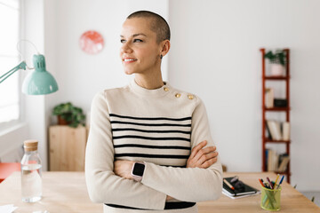 Successful portrait of mid adult businesswoman with crossed arms looking away standing at office workplace