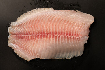 Fresh tilapia fillet on black background, top view.