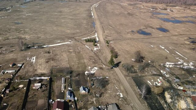 Flying over the village and empty fields with a backwater in early spring