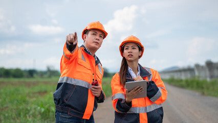 Two people wearing orange safety gear are looking at a tablet