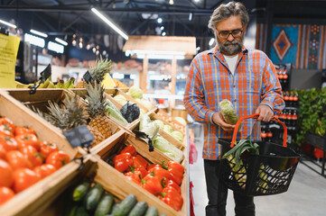 Stylish senior man in red shirt choosing vegetables and fruits at supermarket