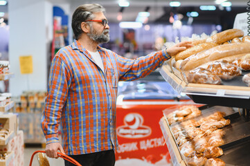 Senior man choosing groceries bread from shelf in supermarket. Bakery and grocery stores