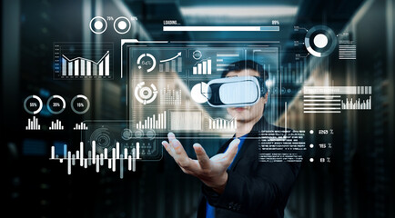 Project manager holding financial hologram while wearing VR glasses at data center. Professional business man looking and accessing at marketing data by using augmented reality technology. Ingenuity.