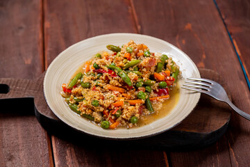 Couscous with vegetables in sauce on a plate on the table next to a fork