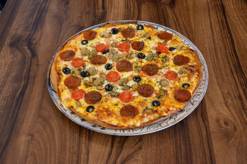 A pizza with pepperoni, olives, and mushrooms sits on a wooden table