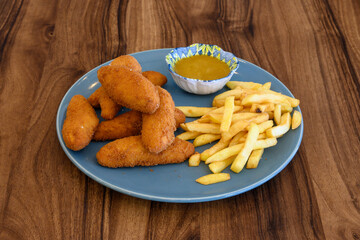 A plate of fried chicken and french fries sits on a wooden table
