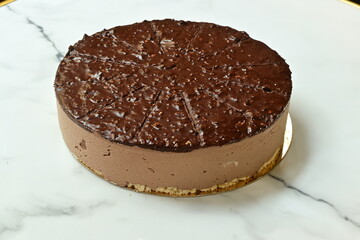 A chocolate cake with nuts on top sits on a marble counter