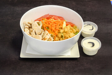 A salad with chicken and carrots is served in a white bowl