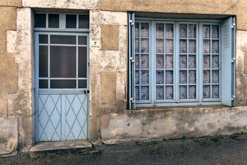 Obraz premium Vintage wooden door with ornate metal grille and closed window shutters on a stone wall facade.For the background of your photos and collages