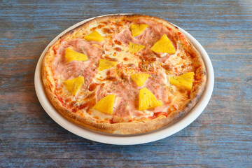 A pizza with pineapple and ham on it sits on a white plate