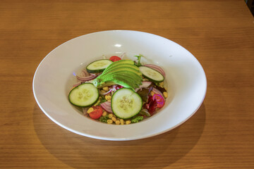 A white bowl of salad with cucumbers, tomatoes, and avocado