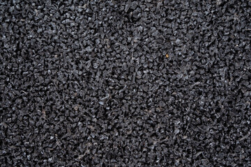 This is a closeup view of black rubber granules, which are ideal for use in sports flooring and playground surfaces. They ensure both safety and durability for users