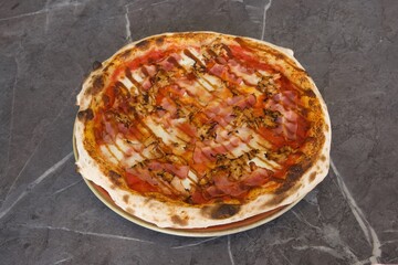 A pizza with ham and cheese on it sits on a plate