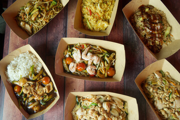 A variety of Asian food is displayed in paper containers on a wooden table