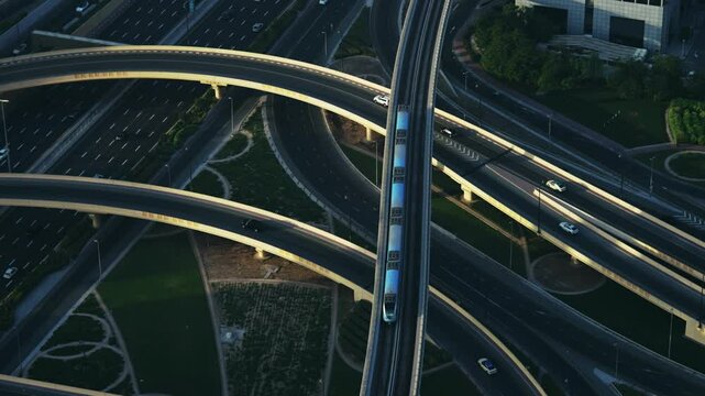 Dubai metro train drive on elevated tracks over highway junction interchange amidst the modern cityscape of Dubai downtown at sunset, no logos