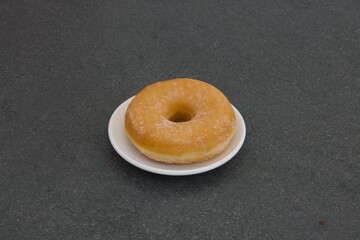 A donut sits on a white plate on a black counter