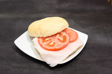 A sandwich with a tomato slice on top of a white plate