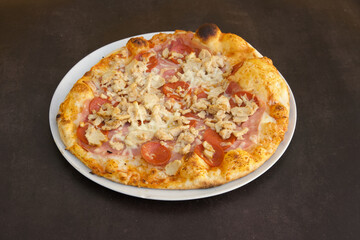 A pizza with pepperoni and chicken on it sits on a white plate