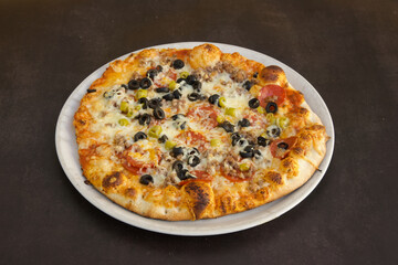A pizza with olives, cheese, and pepperoni sits on a white plate