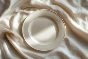 A simple, elegant white plate rests on a creamy fabric, bathed in soft sunlight.