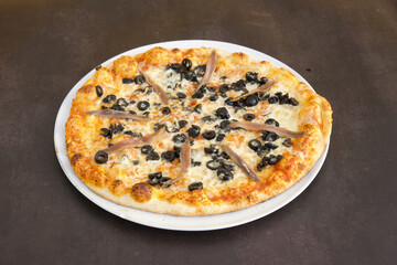 A pizza with olives and anchovies on it sits on a white plate