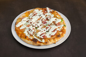 A pizza with ham and cheese on a white plate