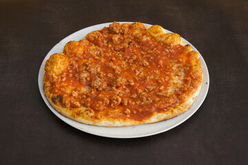 A pizza with meat toppings sits on a white plate