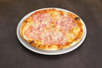 A pizza with ham and cheese sits on a white plate