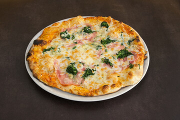 A pizza with ham and spinach on a white plate