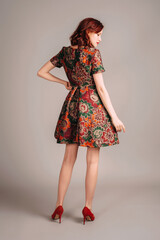 Studio portrait of beautiful redhead young woman walking in brown evening gown and red high heels....