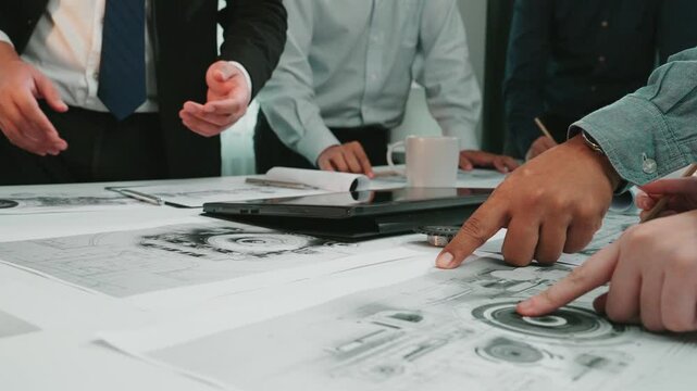 A diverse team collaborates on a technical project, discussing blueprints and using a tablet in a modern office to foster creativity and innovation. SACTR