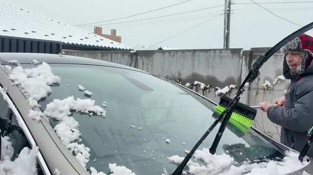A Happy man cleaning snow from car in winter on street near home