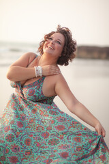 A beautiful fat girl in a summer Indian sundress walks along the sandy shore of the ocean