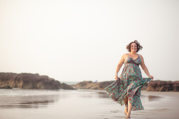 A beautiful fat girl in a summer Indian sundress walks along the sandy shore of the ocean